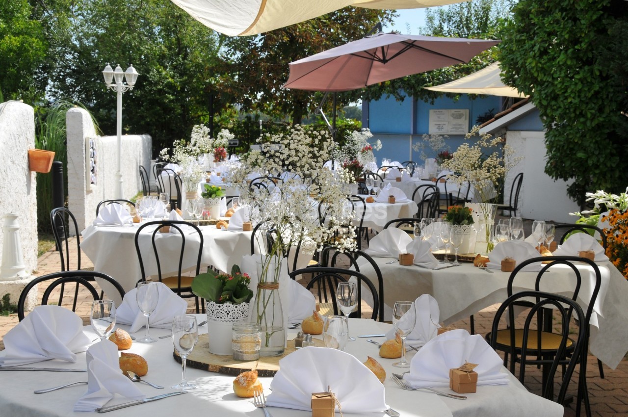 Terrasse d'un restaurant avec des tables dressées, nappes blanches, serviettes pliées et décorations florales.