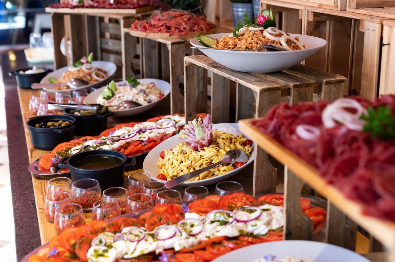 Buffet varié avec salades, charcuteries, tomates, mozzarella et condiments disposés sur des caisses en bois.