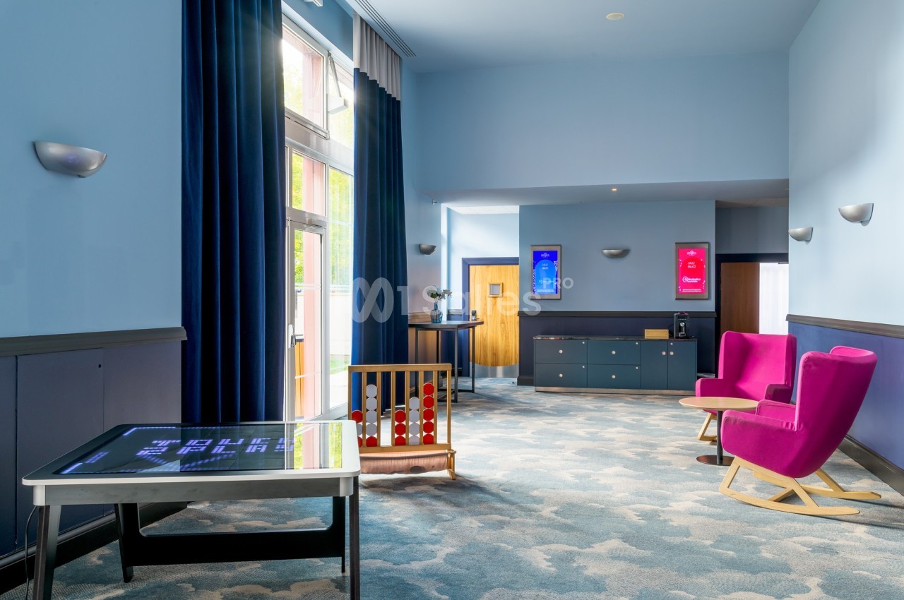 Espace lumineux avec fauteuils roses, table interactive, jeux pour enfants et affiches colorées sur les murs bleus.