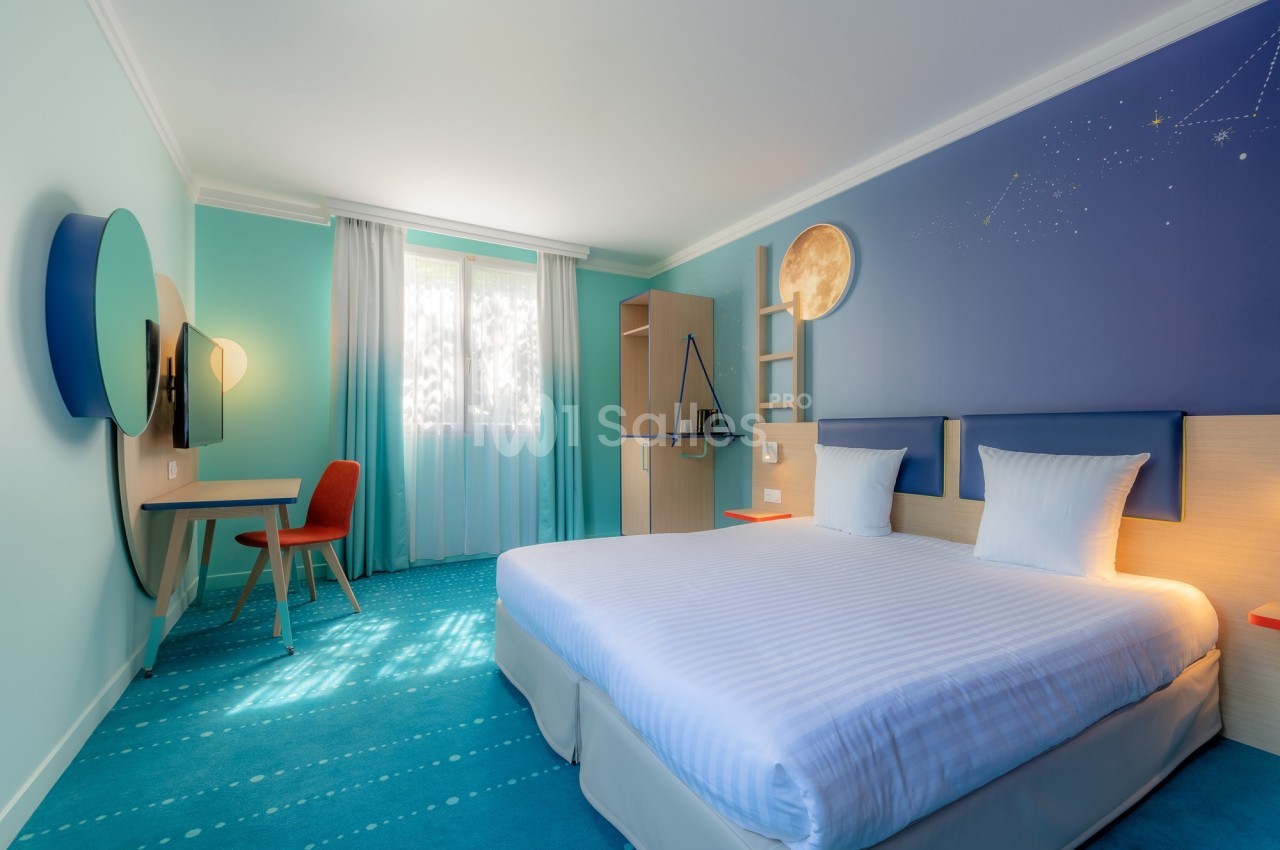 Chambre d'hôtel lumineuse avec un lit double, un bureau, une chaise rouge et une décoration murale sur le thème de l'espace.