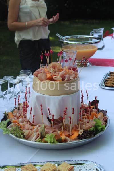 Plateau de charcuterie et melon présenté avec des pics, entouré de salades sur une table de buffet en extérieur.