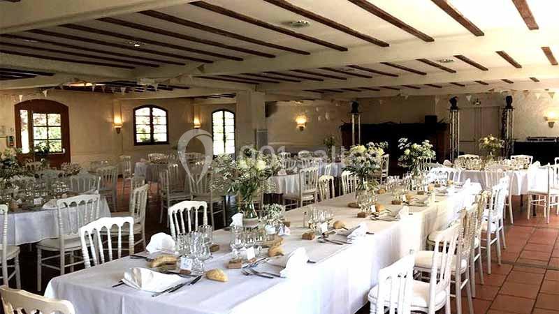 Salle de réception lumineuse avec tables dressées, nappes blanches, chaises assorties et décorations florales.