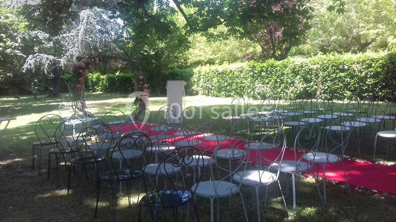 Chaises en métal disposées autour d'une allée rouge dans un jardin, préparées pour une cérémonie en plein air.