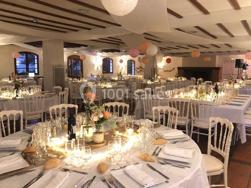 Salle de réception décorée avec des tables rondes dressées, éclairage chaleureux et suspensions colorées au plafond.