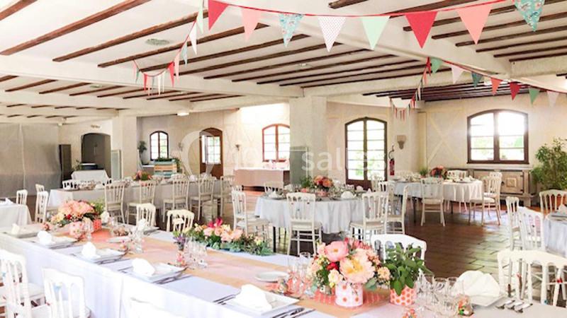Salle de réception lumineuse décorée de guirlandes et de fleurs, avec des tables dressées pour un événement.