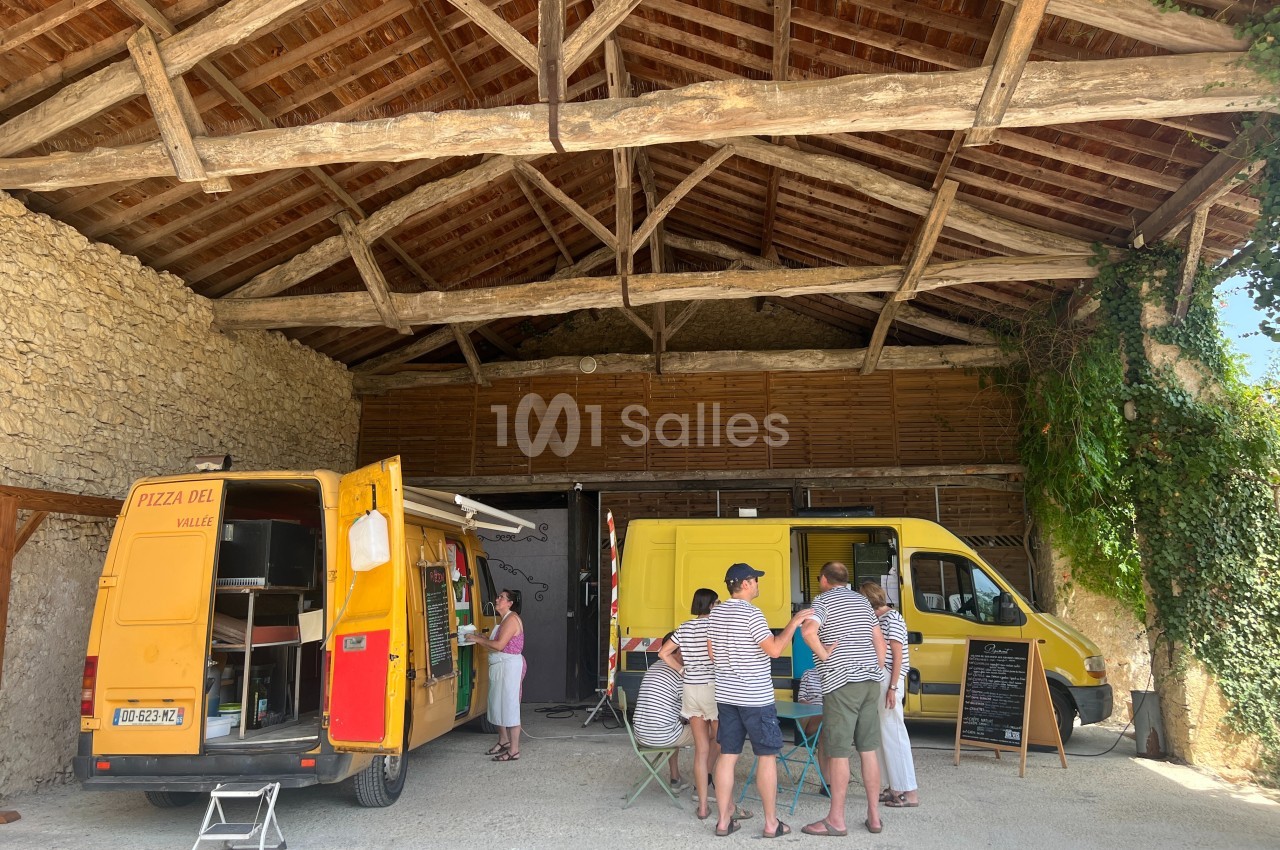 Deux camions jaunes de pizza stationnés sous un hangar en bois, avec des clients attendant leur commande.