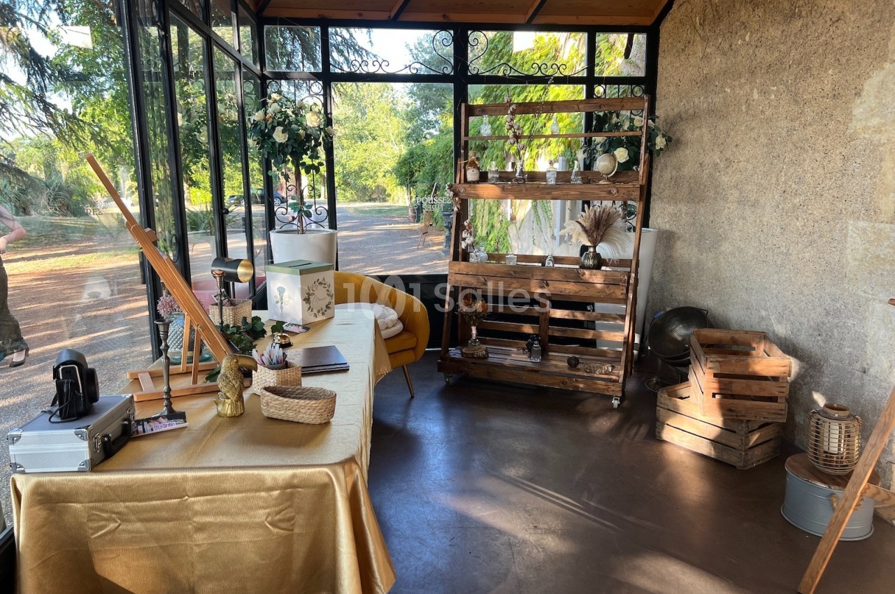 Espace décoré avec une table recouverte d'une nappe dorée, étagères en bois et éléments rustiques près d'une baie vitrée.