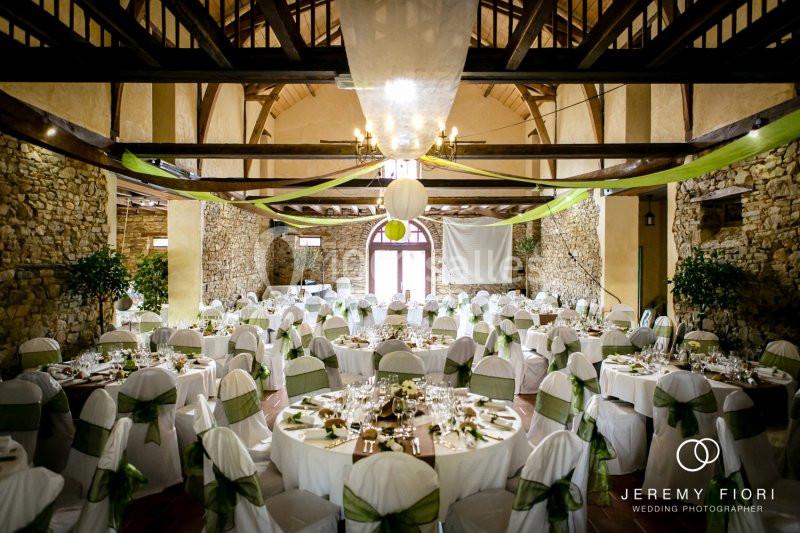 Salle de réception décorée pour un mariage, avec des tables rondes, nappes blanches et rubans verts.