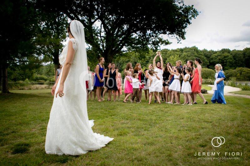 Une mariée en robe blanche regarde un groupe de femmes attraper son bouquet lancé dans un parc verdoyant.