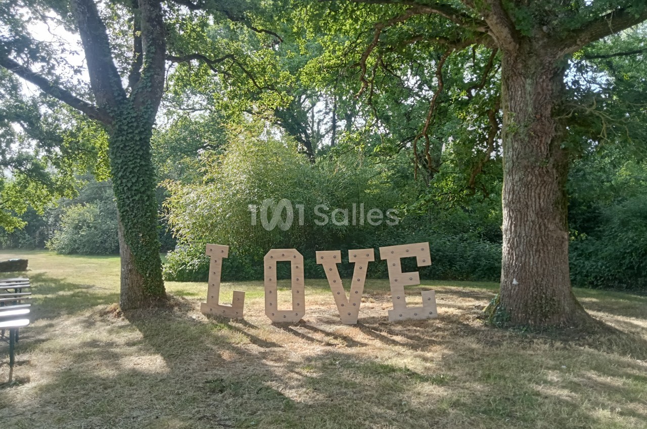 Lettres géantes formant le mot ’LOVE’ installées entre deux arbres dans un espace vert ensoleillé.