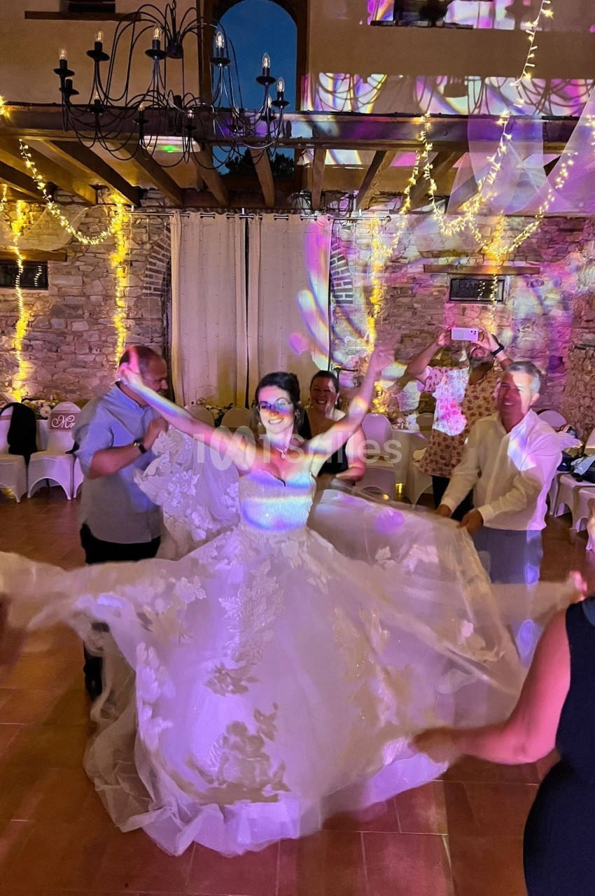 Une mariée danse au centre d'une salle décorée de guirlandes lumineuses, entourée d'invités.