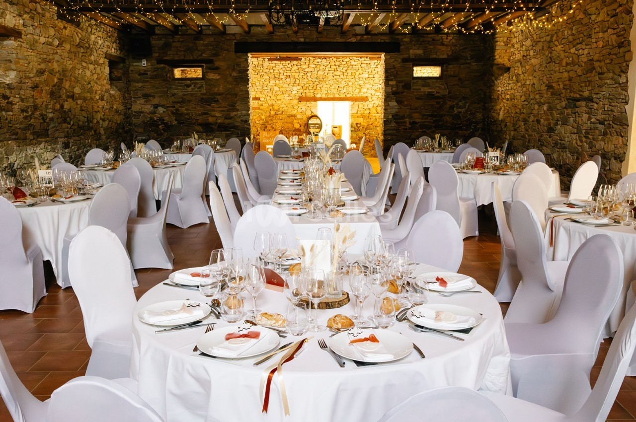 Salle de réception décorée avec des tables rondes dressées, nappes blanches et guirlandes lumineuses suspendues.