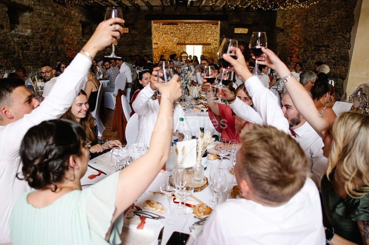 Des convives lèvent leurs verres autour d'une grande table lors d'un repas festif dans une salle en pierre.
