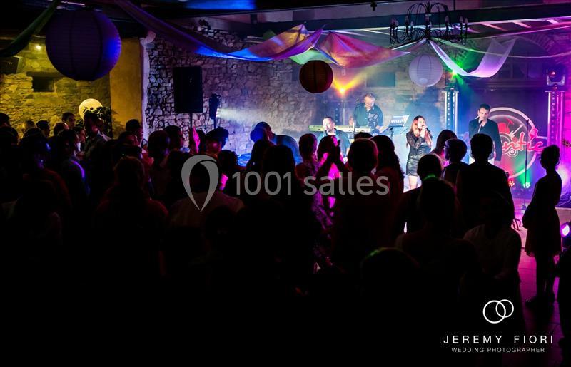 Groupe musical jouant sur scène devant une foule dans une salle éclairée par des lumières colorées.