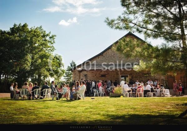 Groupe de personnes assises à l'extérieur devant un bâtiment en pierre, entouré de verdure et d'arbres.