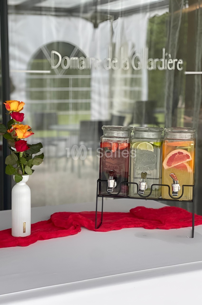 Distributeurs de boissons aromatisées et vase avec roses sur une table décorée d’un chemin de table rouge.