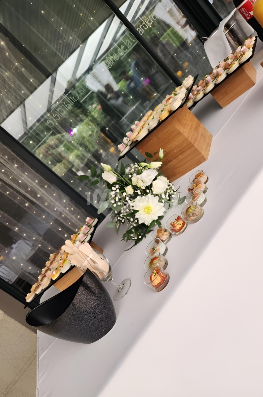 Table décorée avec des fleurs blanches, des verrines et des amuse-bouches disposés sur des présentoirs en bois.