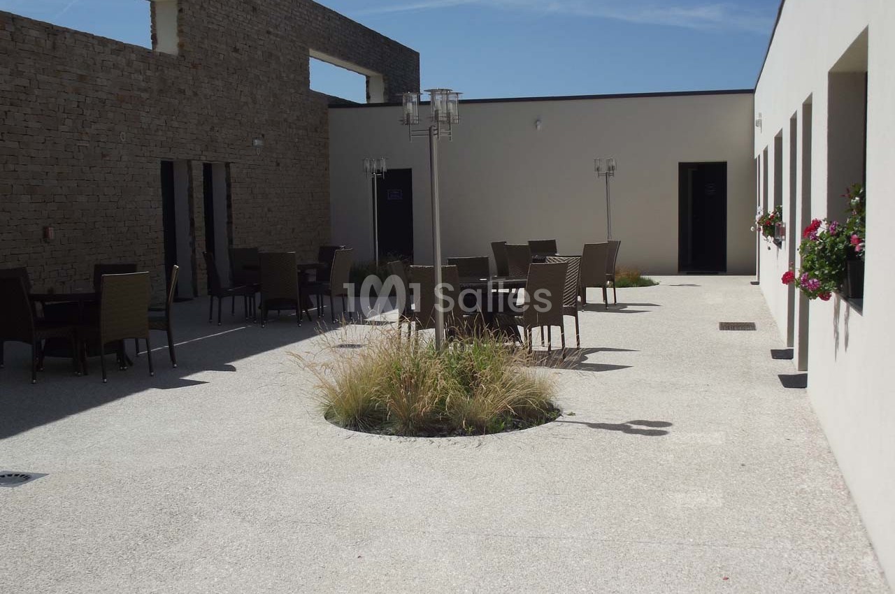 Cour intérieure avec mobilier de jardin, murs clairs, plantes décoratives et ciel dégagé en arrière-plan.