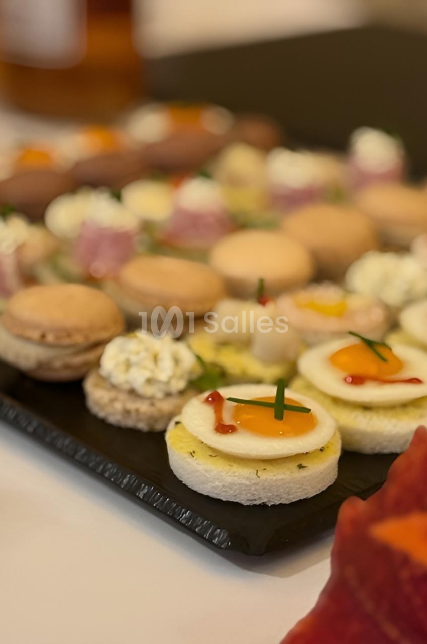 Plateau de canapés variés avec œufs de caille, macarons salés et autres amuse-bouches sur une table.
