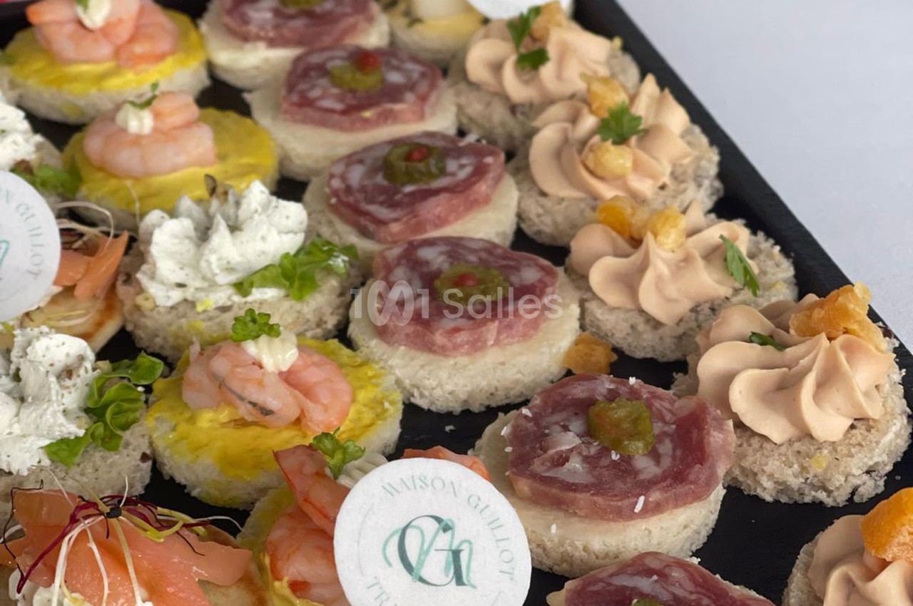 Plateau de canapés variés avec crevettes, saumon, mousse et charcuterie, décorés de garnitures fraîches.