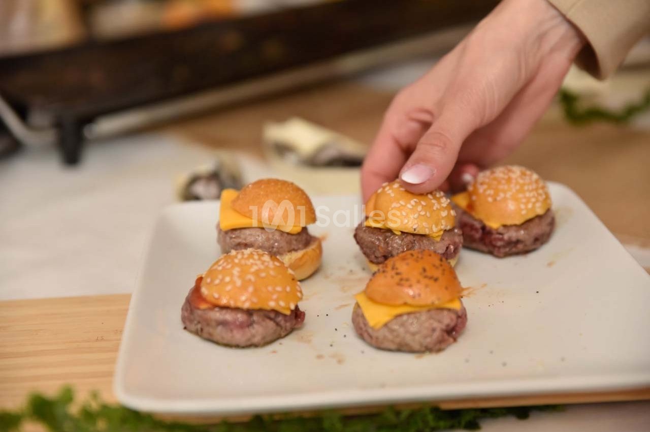 Assiette de mini-burgers garnis de fromage avec une main en train d'en saisir un.