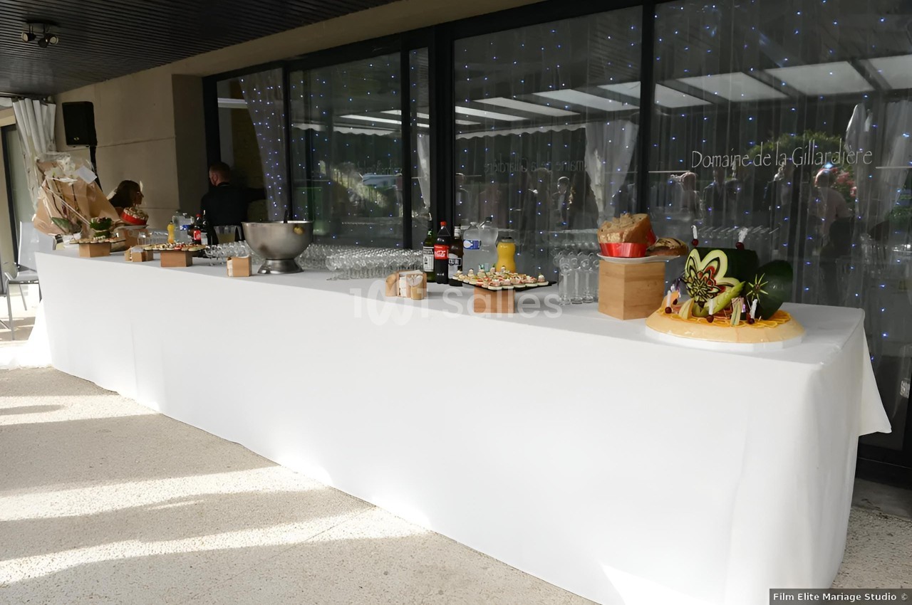 Table de buffet dressée avec nappes blanches, boissons, plats variés et décorations, devant une baie vitrée.