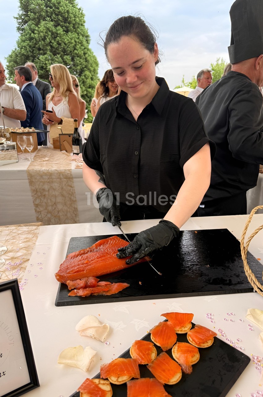 Une femme découpe du saumon fumé sur une planche lors d'un événement en plein air.