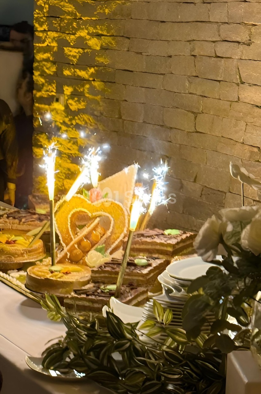 Table décorée avec des desserts, pièce montée en forme de cœur et fontaines lumineuses allumées, devant un mur en pierre.