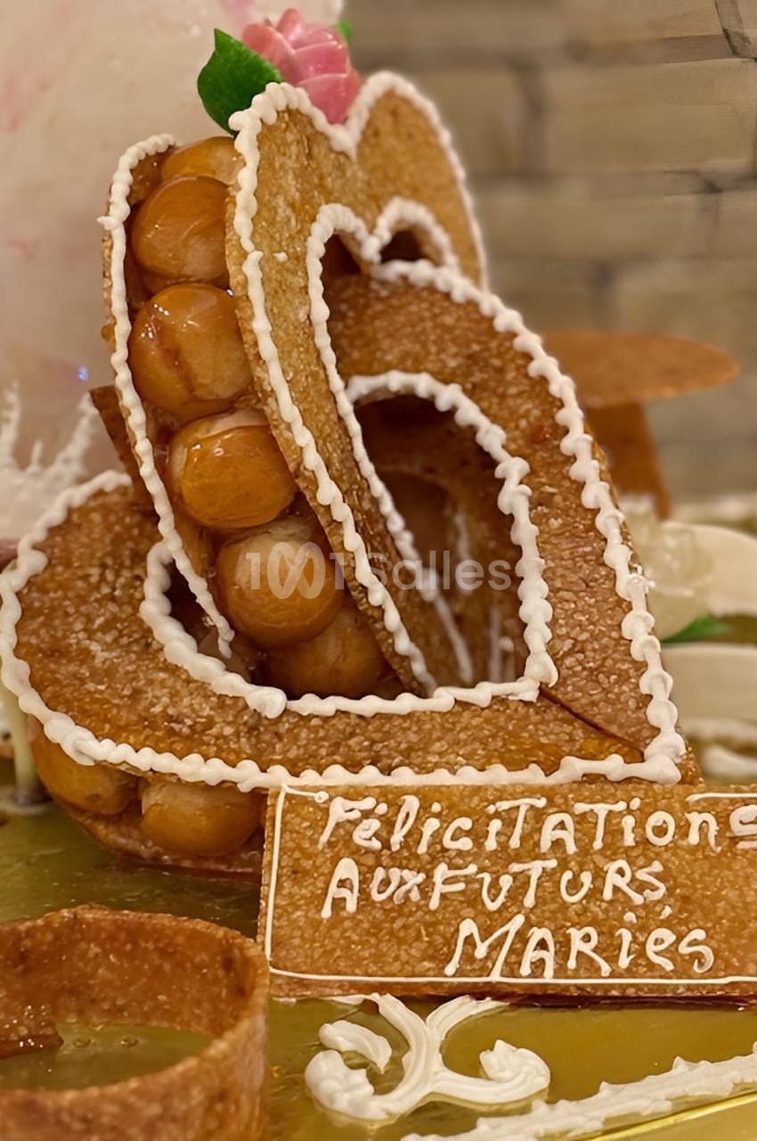 Pièce montée en forme de cœur avec des choux et du caramel, décorée d’un message ’Félicitations aux futurs mariés’.