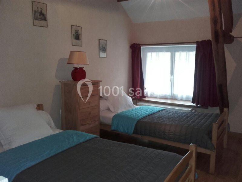 Chambre avec deux lits simples, une commode en bois, une lampe rouge et une fenêtre avec rideaux rouges.
