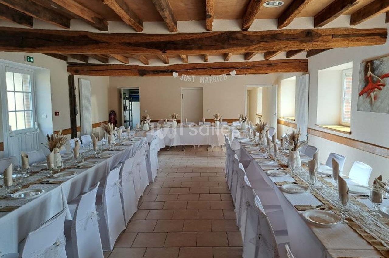 Salle de réception décorée pour un mariage, avec de longues tables dressées et une bannière ’Just Married’.