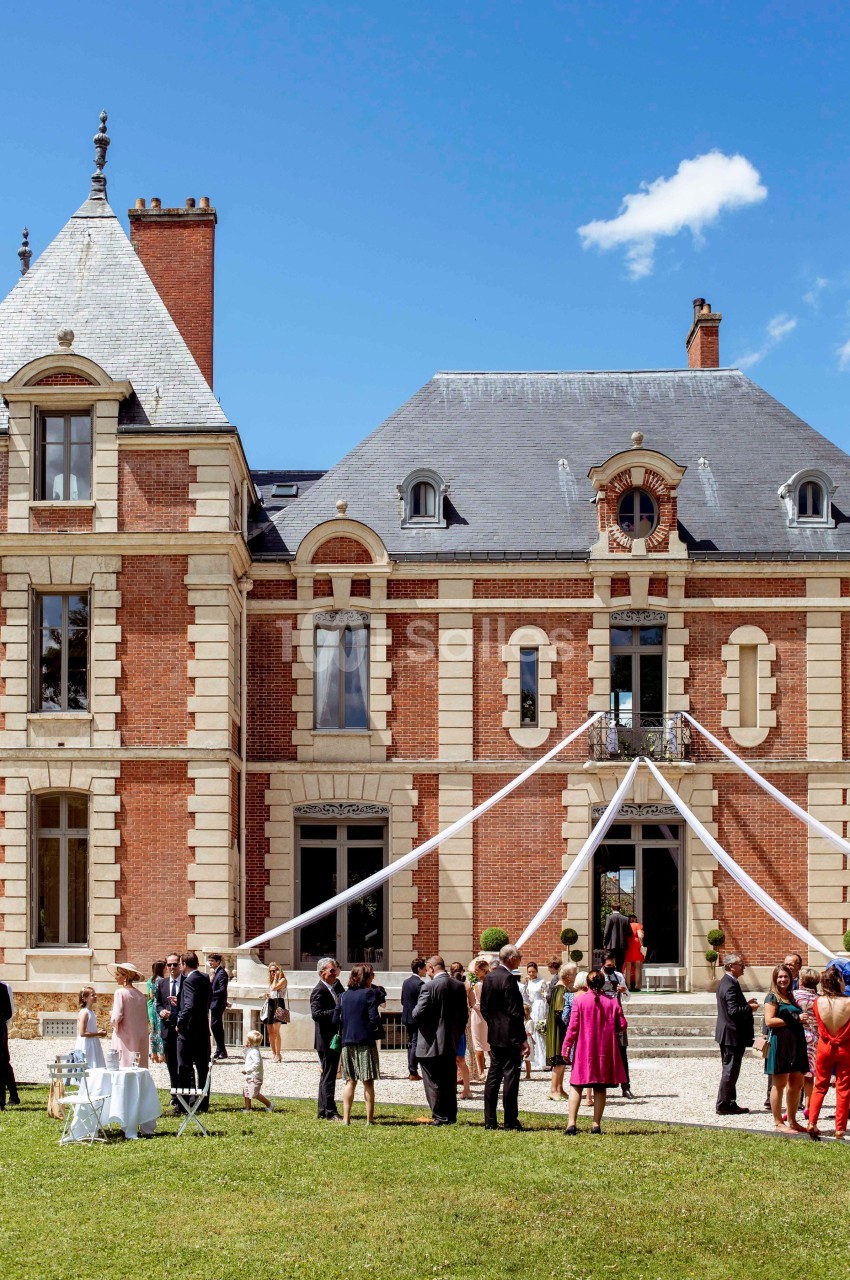 Groupe de personnes rassemblées devant un château en briques rouges lors d'un événement sous un ciel dégagé.