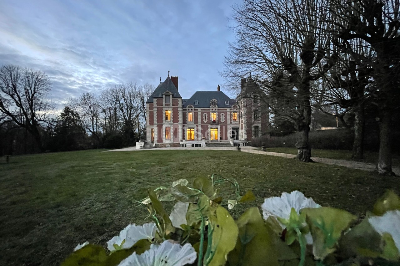 Façade d'un château éclairé au crépuscule, vue depuis un parterre de fleurs au premier plan.