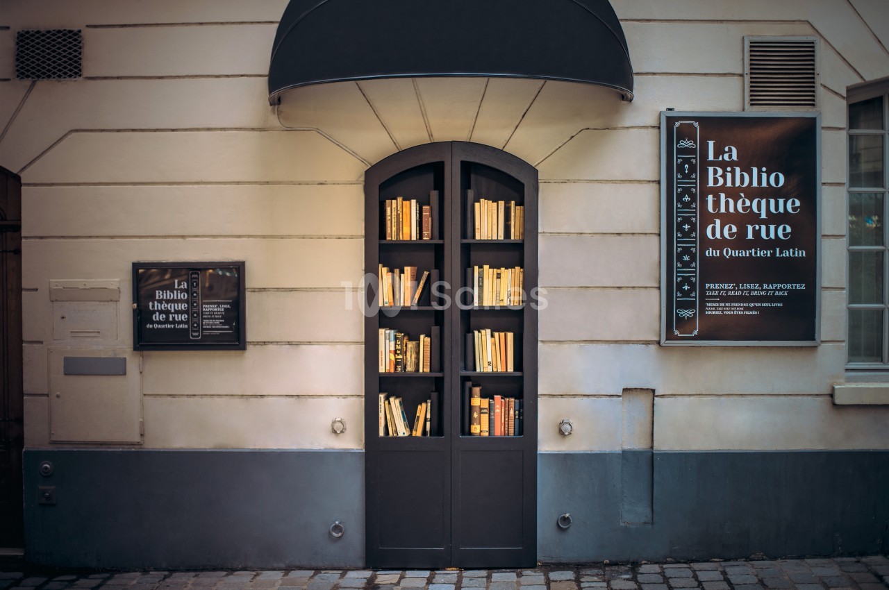 Façade d'une bibliothèque de rue avec des étagères remplies de livres et des panneaux explicatifs sur le mur.