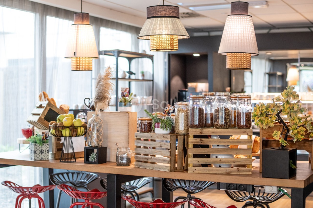 Buffet avec bocaux de céréales, fruits et décorations sur une table en bois, éclairé par des suspensions lumineuses.