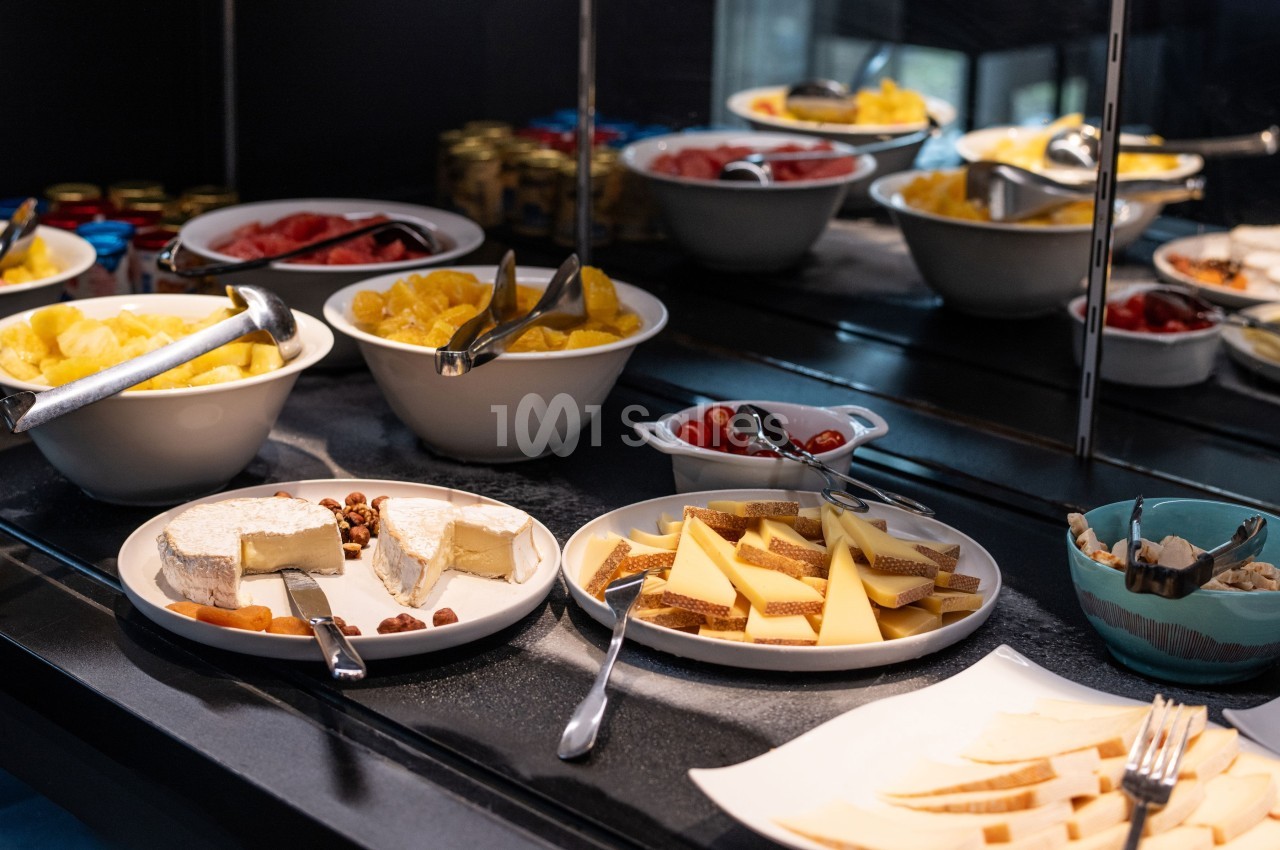 Buffet avec fromages, fruits frais, noix et condiments disposés dans des assiettes et bols sur un comptoir.