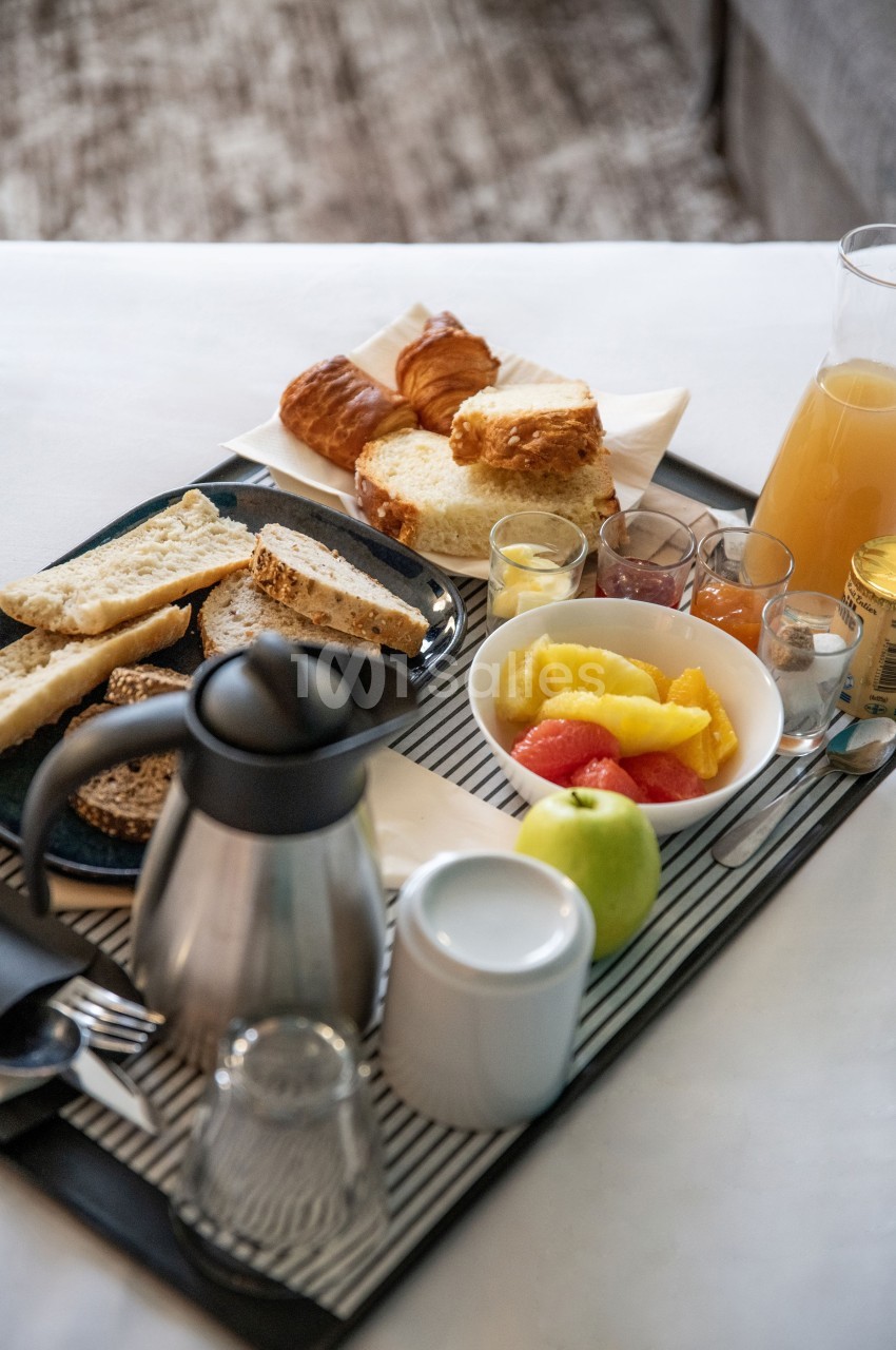 Petit-déjeuner servi sur un plateau avec pain, viennoiseries, fruits, jus d'orange, théière et condiments.