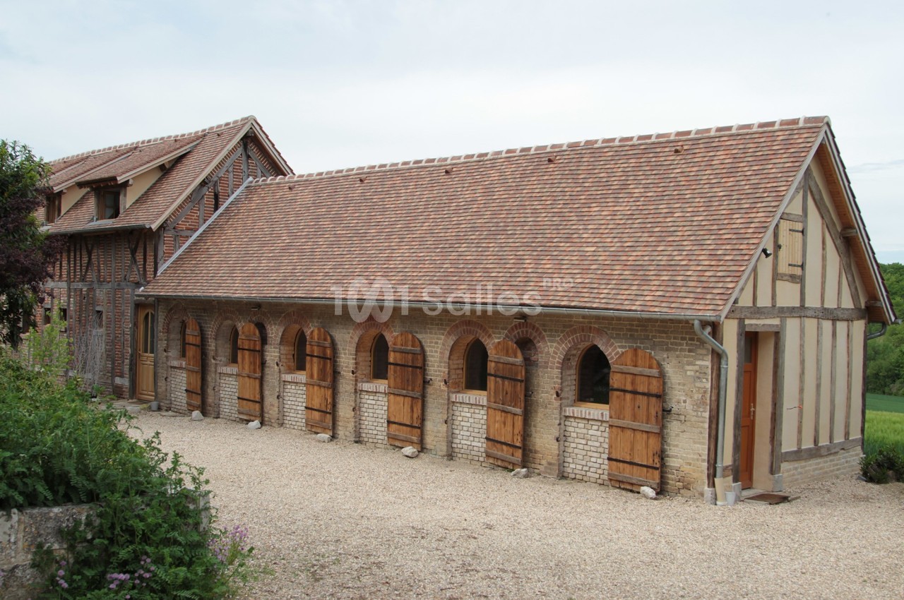 Bâtiment rural en briques et colombages avec toit en tuiles, portes en bois et allée gravillonnée devant.