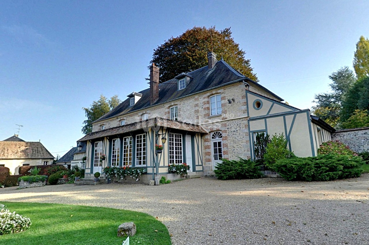 Façade d'une maison traditionnelle à colombages entourée d'un jardin avec allée gravillonnée.