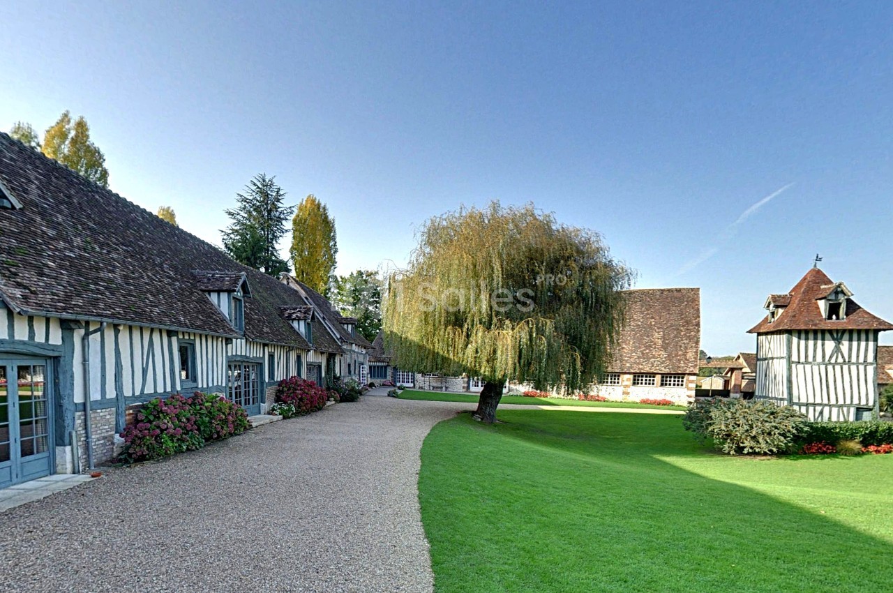 Allée bordée de maisons à colombages, pelouse bien entretenue et un grand saule au centre.