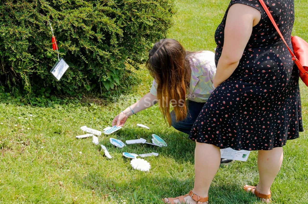 Deux personnes ramassent des objets en plastique éparpillés sur une pelouse près d'un buisson.
