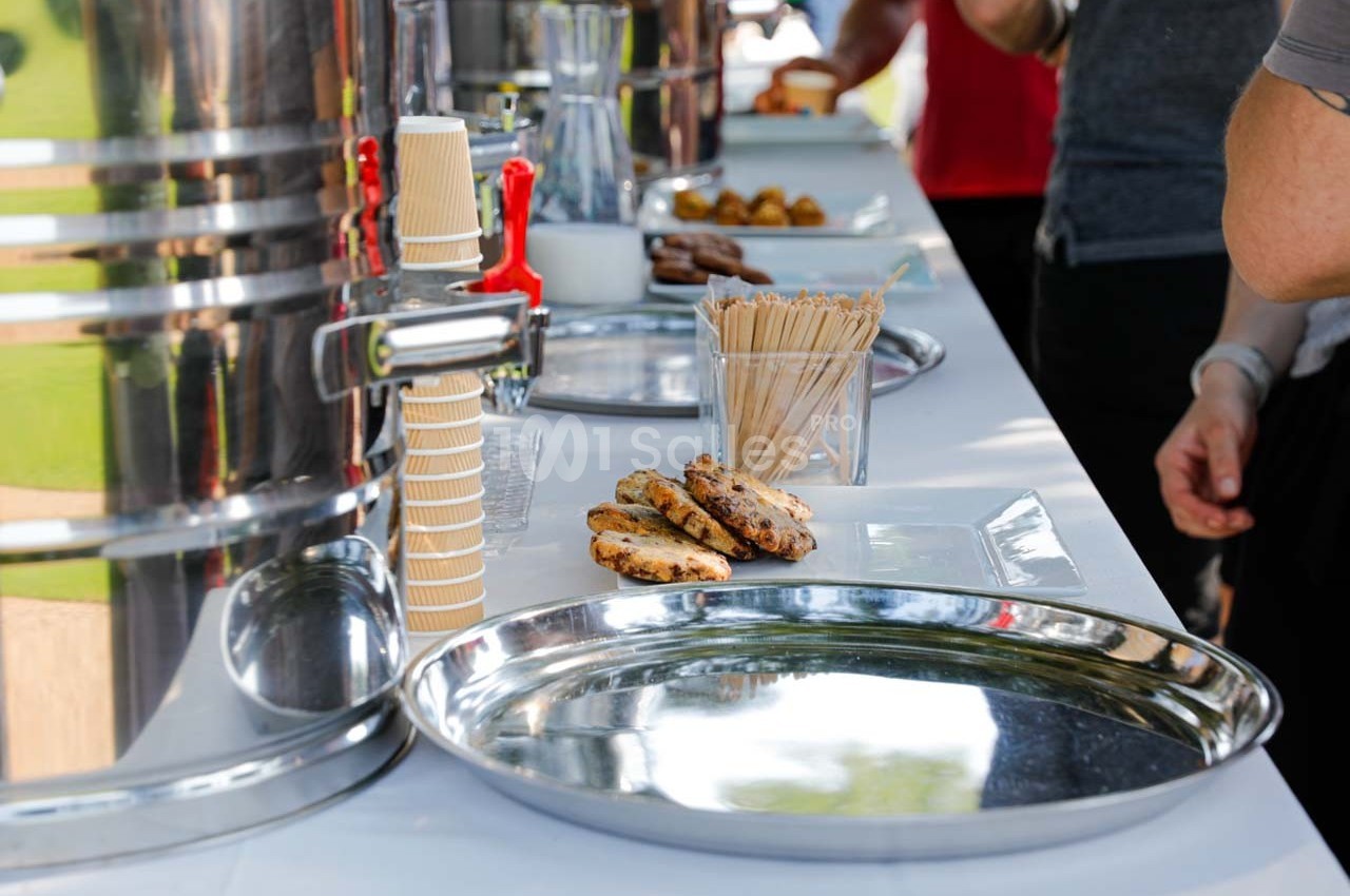 Plateau de biscuits et gobelets en carton sur une table de buffet avec distributeurs de boissons en arrière-plan.