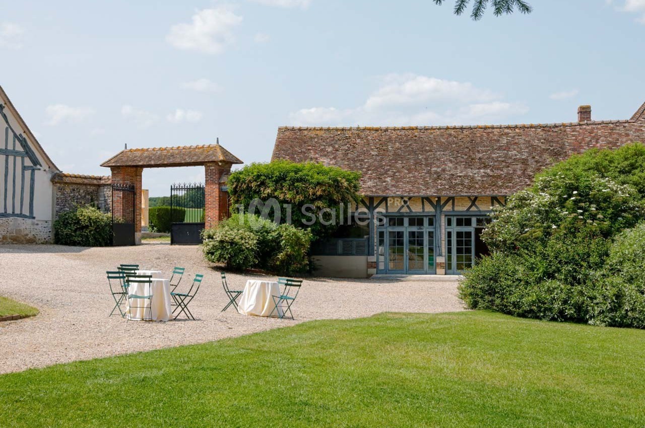 Cour extérieure avec pelouse, mobilier de jardin et bâtiments à colombages sous un ciel dégagé.