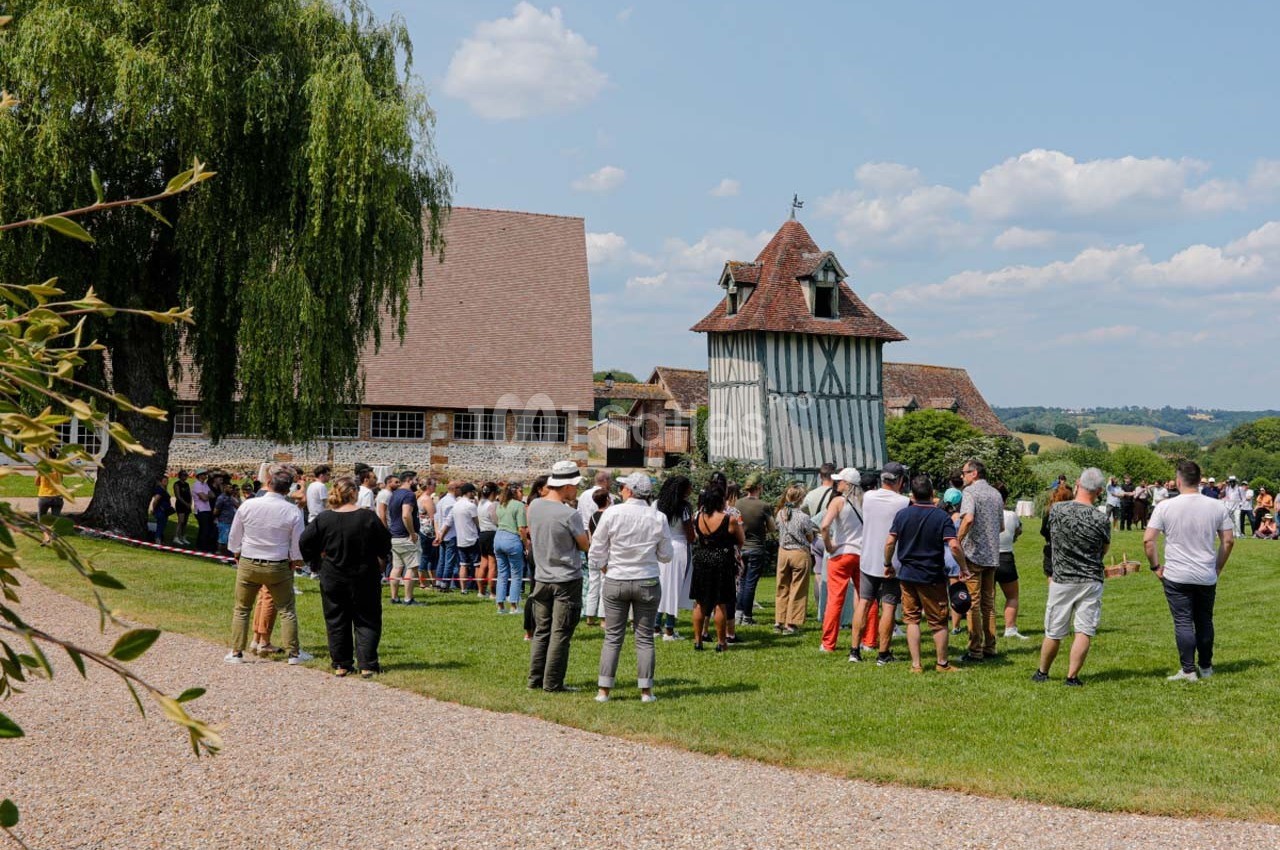 Groupe de personnes rassemblées en plein air devant des bâtiments à colombages dans un cadre champêtre.
