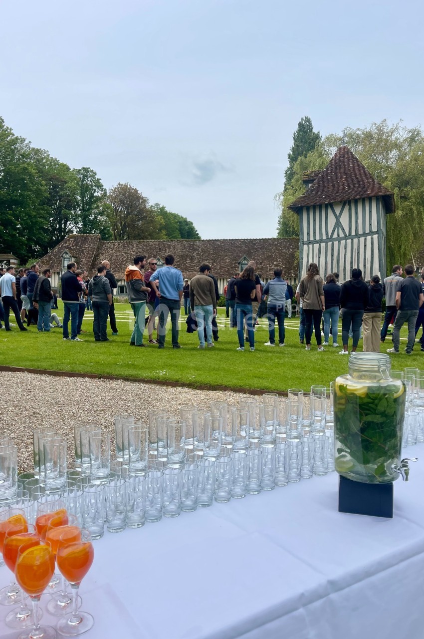 Groupe de personnes rassemblées dans un jardin près d'un bâtiment à colombages, avec une table dressée au premier plan.