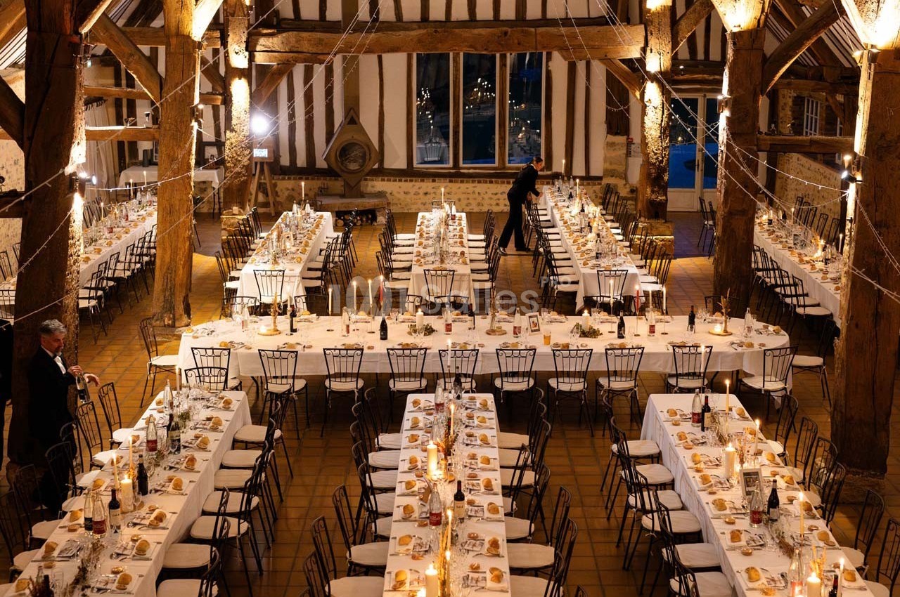 Grande salle de réception avec de longues tables dressées, décorée de lumières suspendues et d'éléments rustiques.