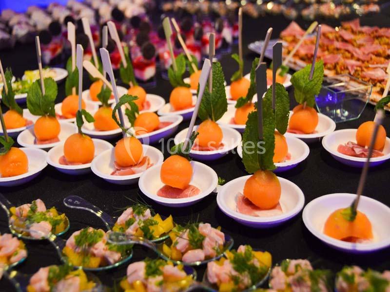 Assortiment de bouchées apéritives comprenant des billes de melon sur brochette et des verrines colorées.