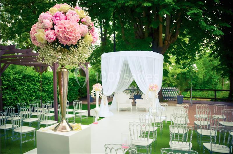 Décoration de mariage en extérieur avec arche blanche, chaises transparentes et compositions florales roses.