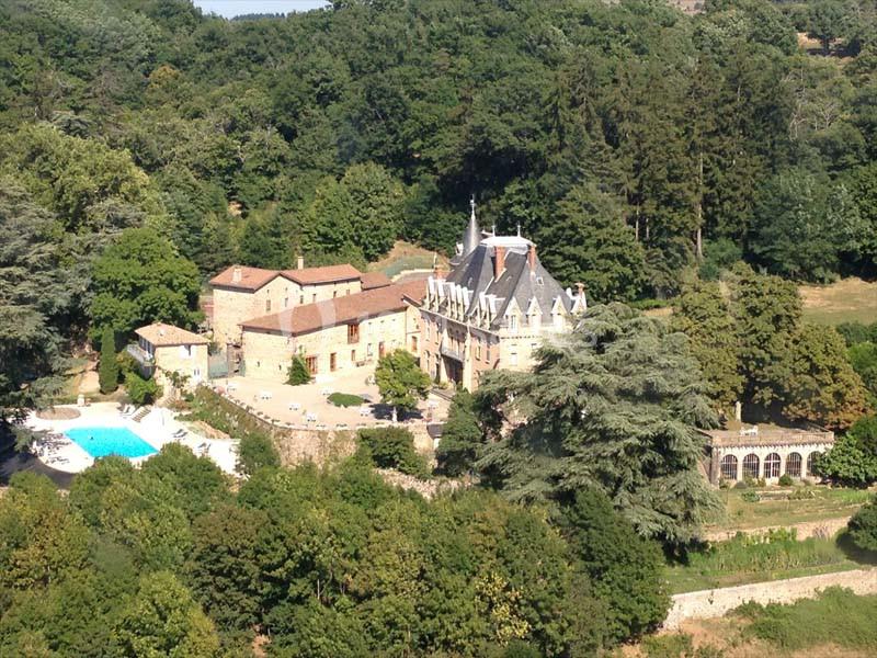 Vue aérienne d'un château entouré de bâtiments annexes, d'une piscine et de végétation dense.