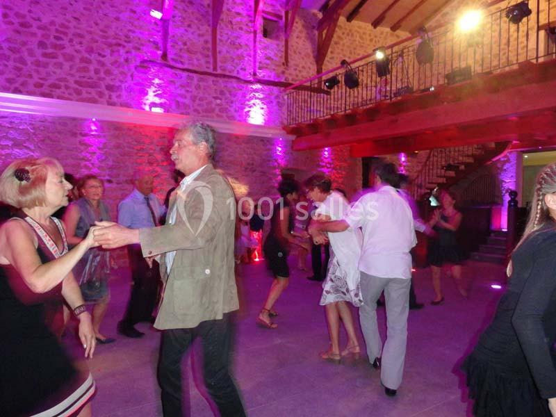 Des personnes dansent dans une salle en pierre éclairée par des lumières colorées, avec une mezzanine en bois.